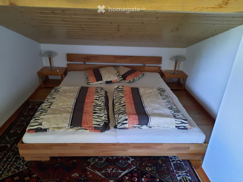 Cozy bedroom with a wooden bed, two nightstands, and lamps. The bed is made with patterned bedding and pillows.