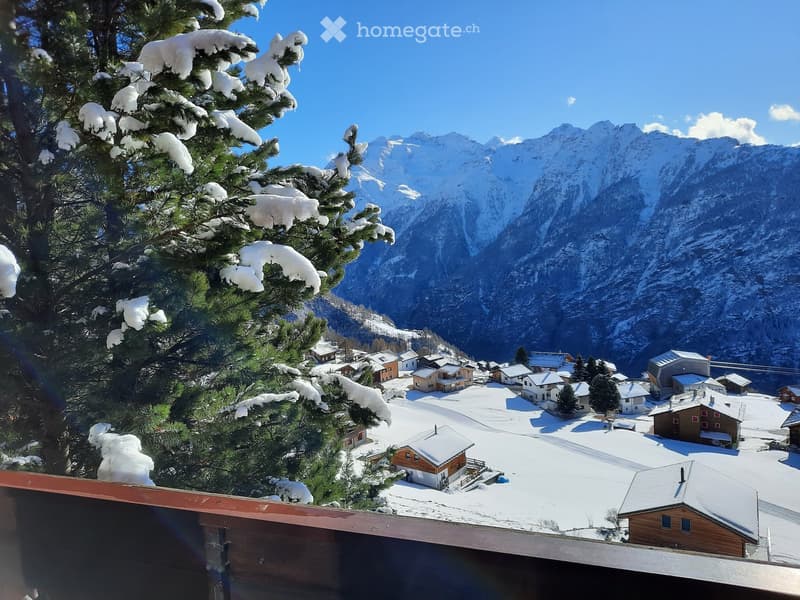 Snow-covered village with wooden houses and snow-covered mountains in the background.