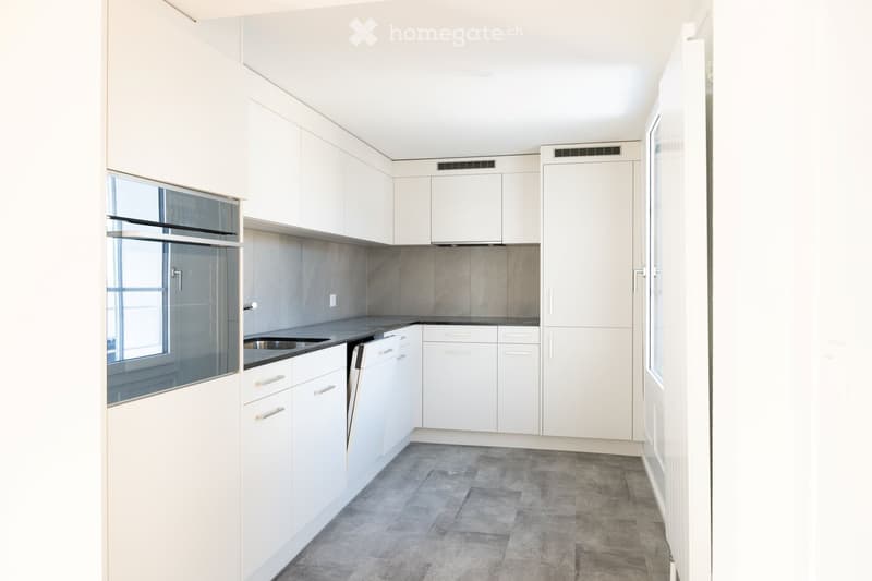 Modern kitchen with white cabinets, stainless steel sink, and dishwasher. Grey tiled backsplash and concrete-style flooring.