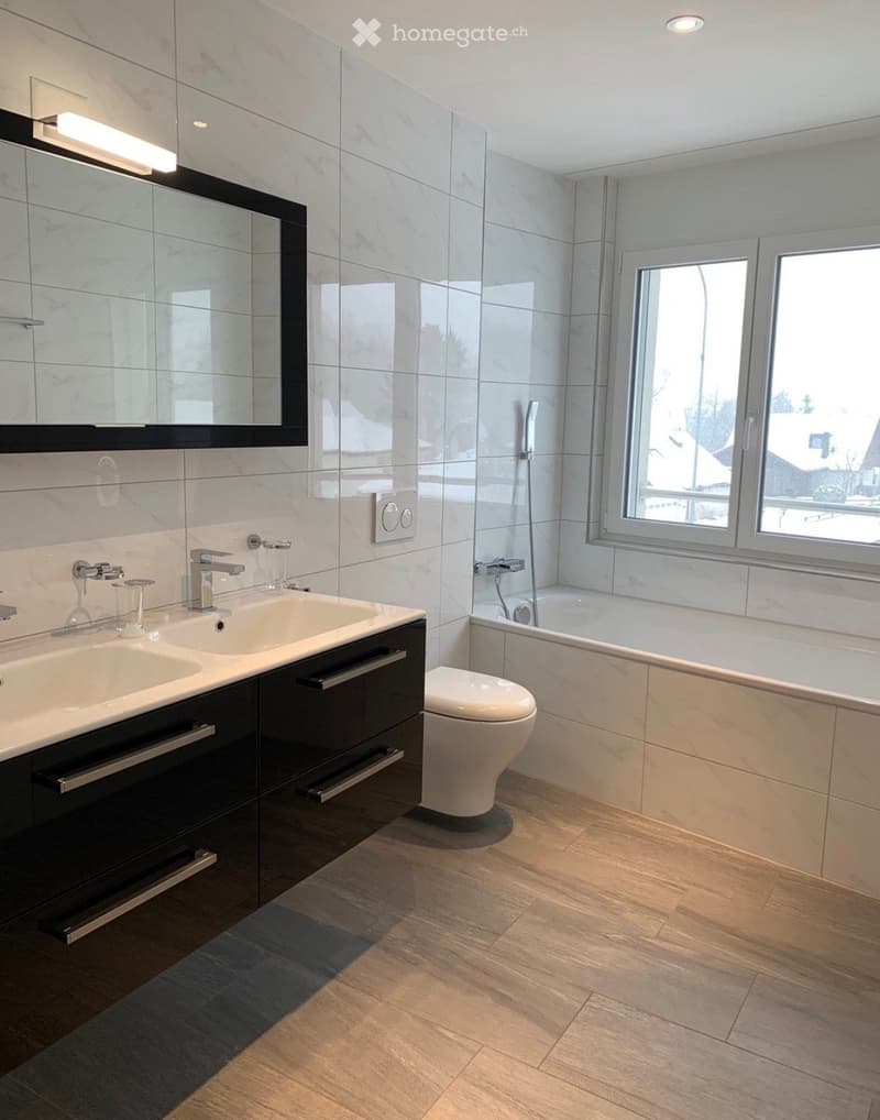 Modern bathroom with double sink, toilet, bathtub, large mirror, and natural light from windows.