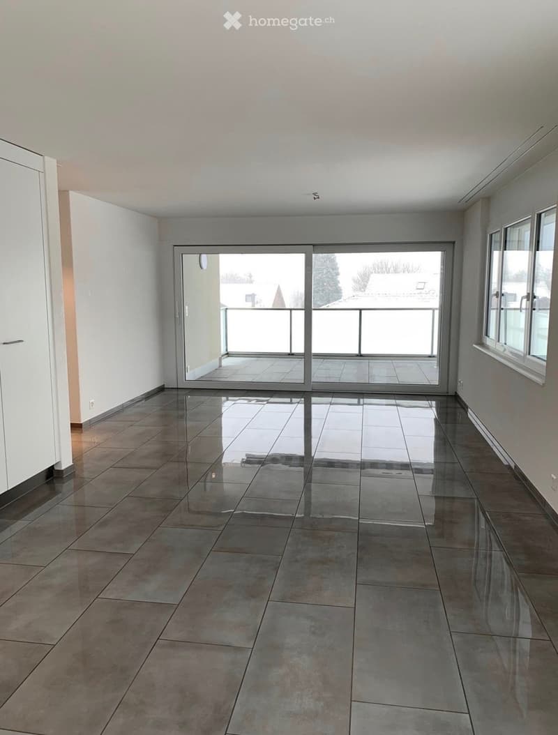 Empty room with tiled floor, large sliding glass door leading to a balcony, and white walls.