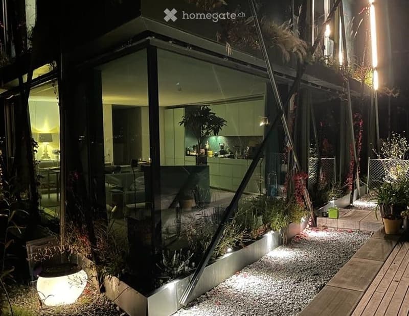 Modern outdoor space with a glass-enclosed patio, featuring a small garden area with potted plants, gravel pathways, and ambient lighting.