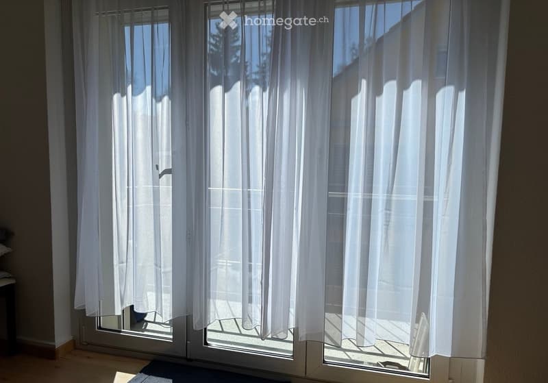 View of a large window with white curtains, showing a clear view of the outside with natural light streaming in.