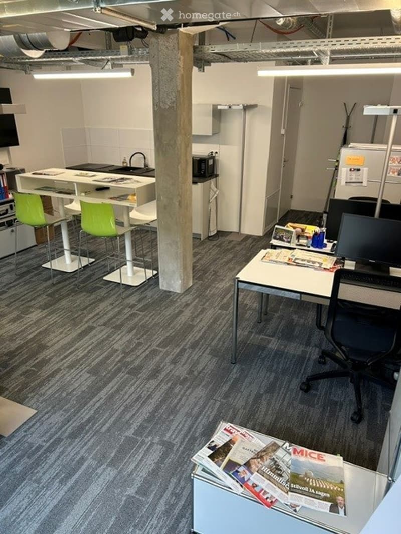 Office space with desks, chairs, stools, a screen, a fridge, a microwave, and a cupboard.
