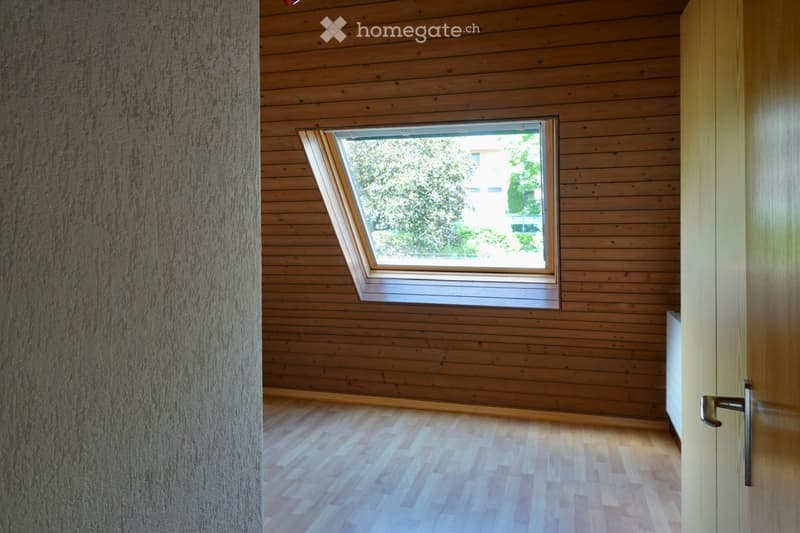 Empty room with wooden walls and floor, featuring a skylight window and a door.
