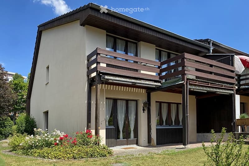Two-story house with a wooden balcony, large windows, and a well-maintained garden.
