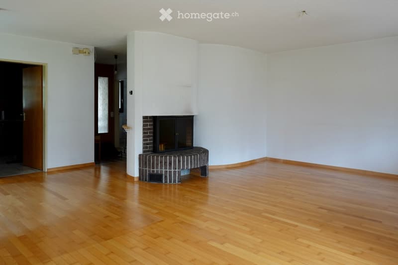 Empty room with wooden flooring, white walls, and a built-in brick fireplace with a black insert.