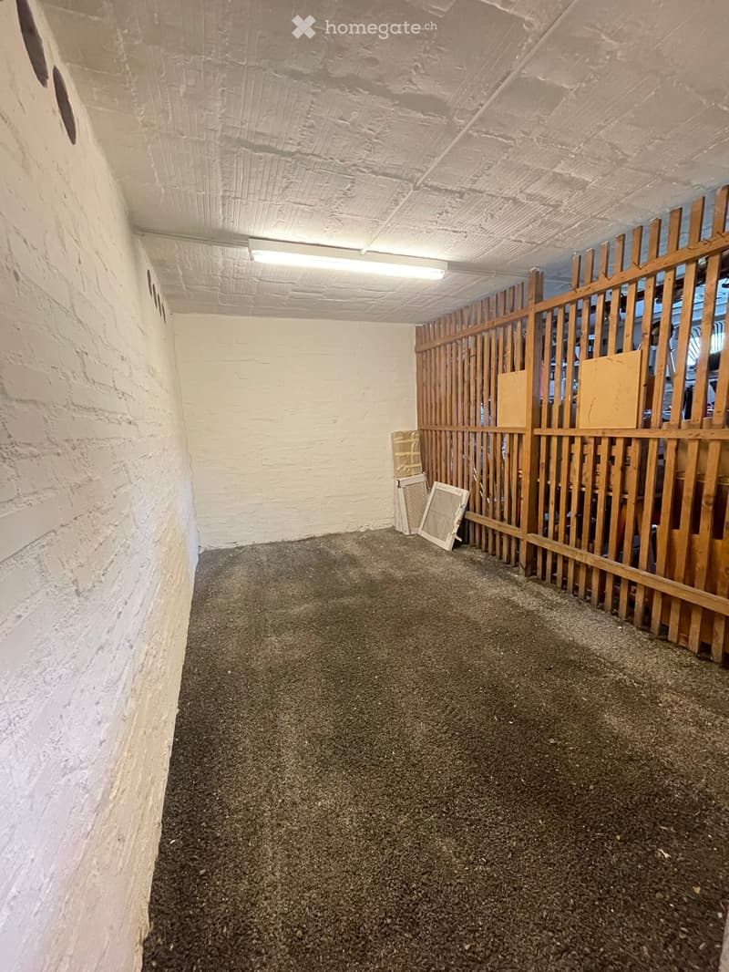 Empty room with concrete floor and white brick walls, featuring a wooden gate and a few scattered items like a screen and a piece of wood.