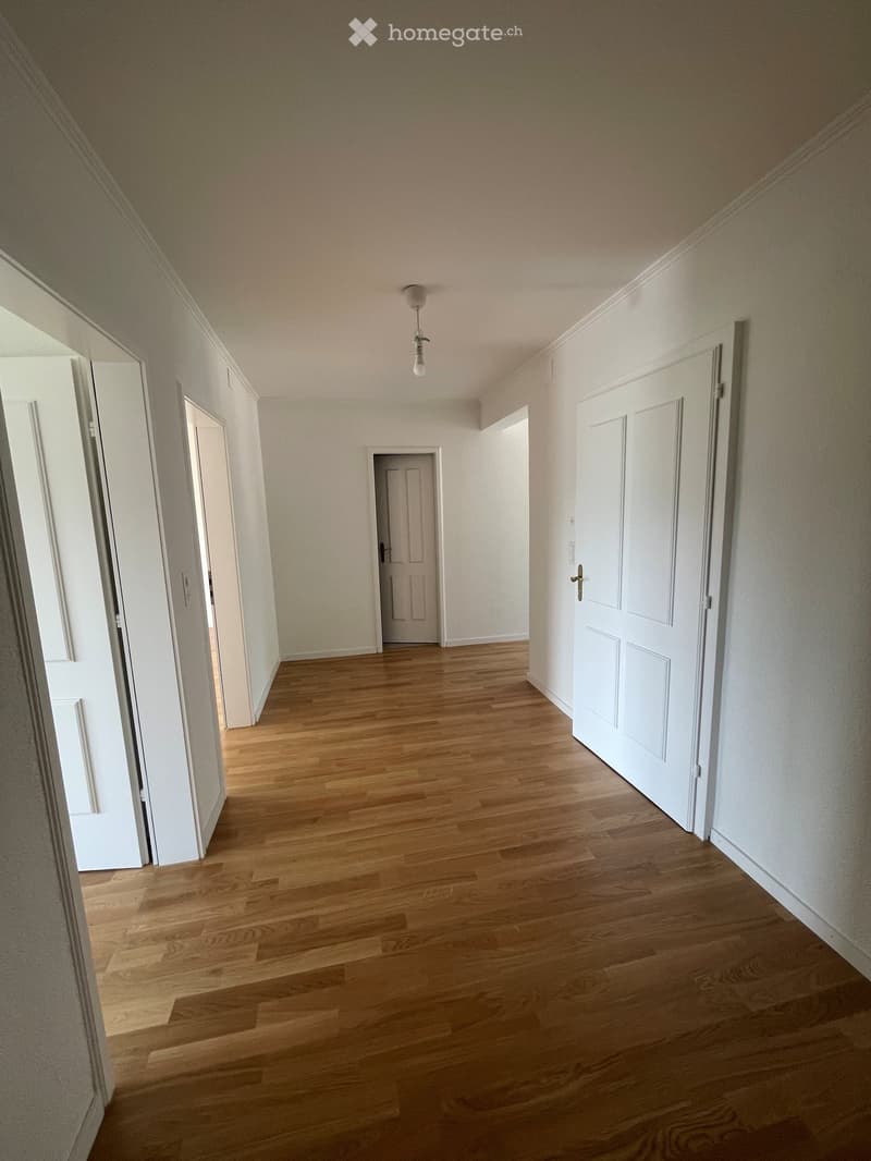 Empty hallway with wooden flooring, white walls, and several closed doors leading to other rooms.