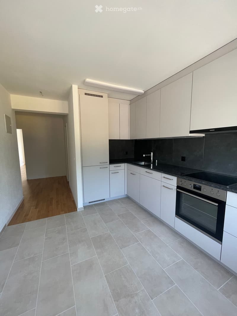 Modern kitchen with white cabinets, a sink, a faucet, and an oven. The floor is tiled, and the walls are painted white.
