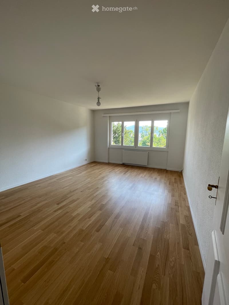 Empty room with wooden flooring, white walls, large windows, and a radiator. No furniture or equipment present.