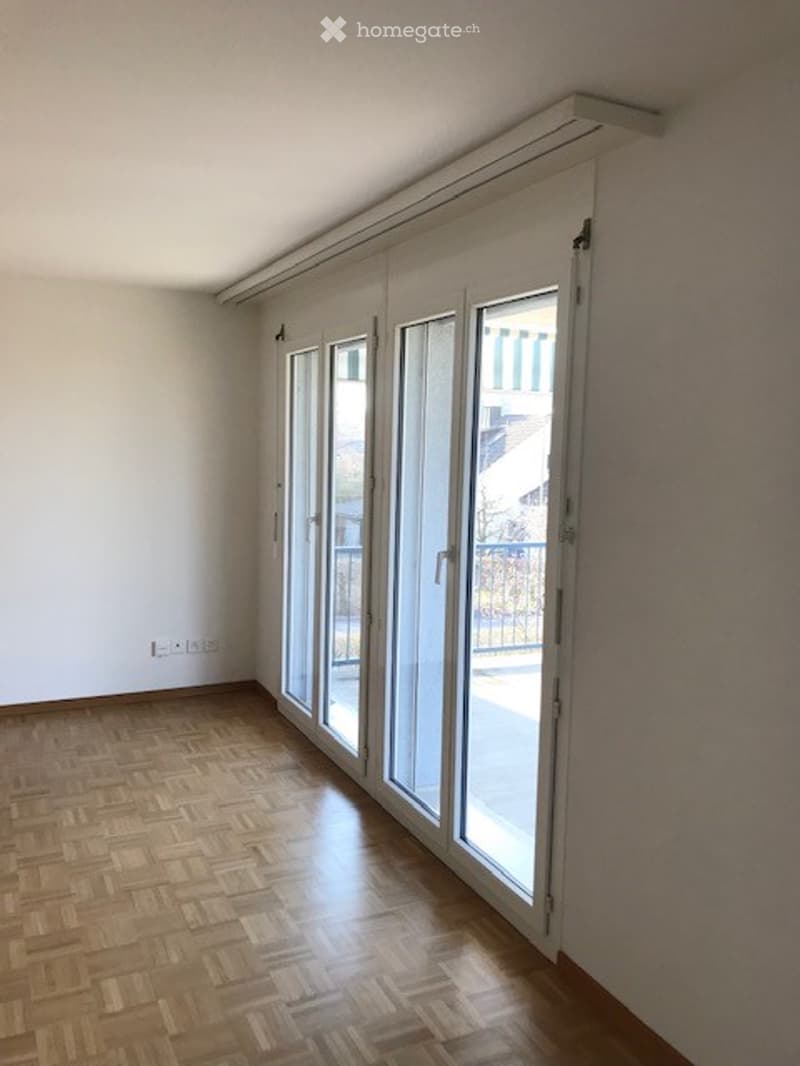Empty room with wooden flooring, large sliding glass doors leading to a balcony, and white walls.
