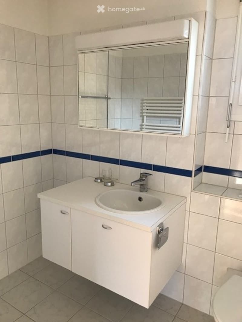 Modern bathroom with white tiles, a white sink cabinet, a mirror above the sink, and a glass shelf on the right side.