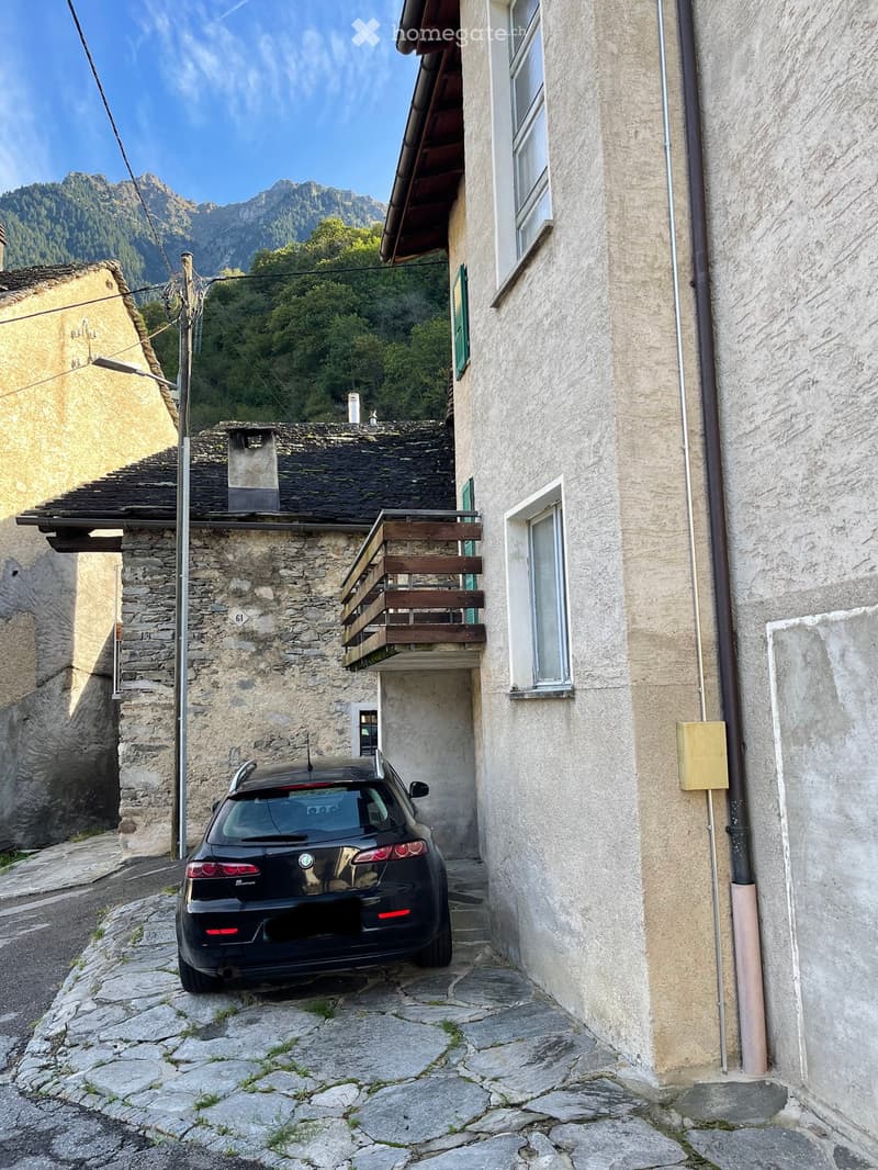 Stone building, black car parked in front, balcony, mountains in the background