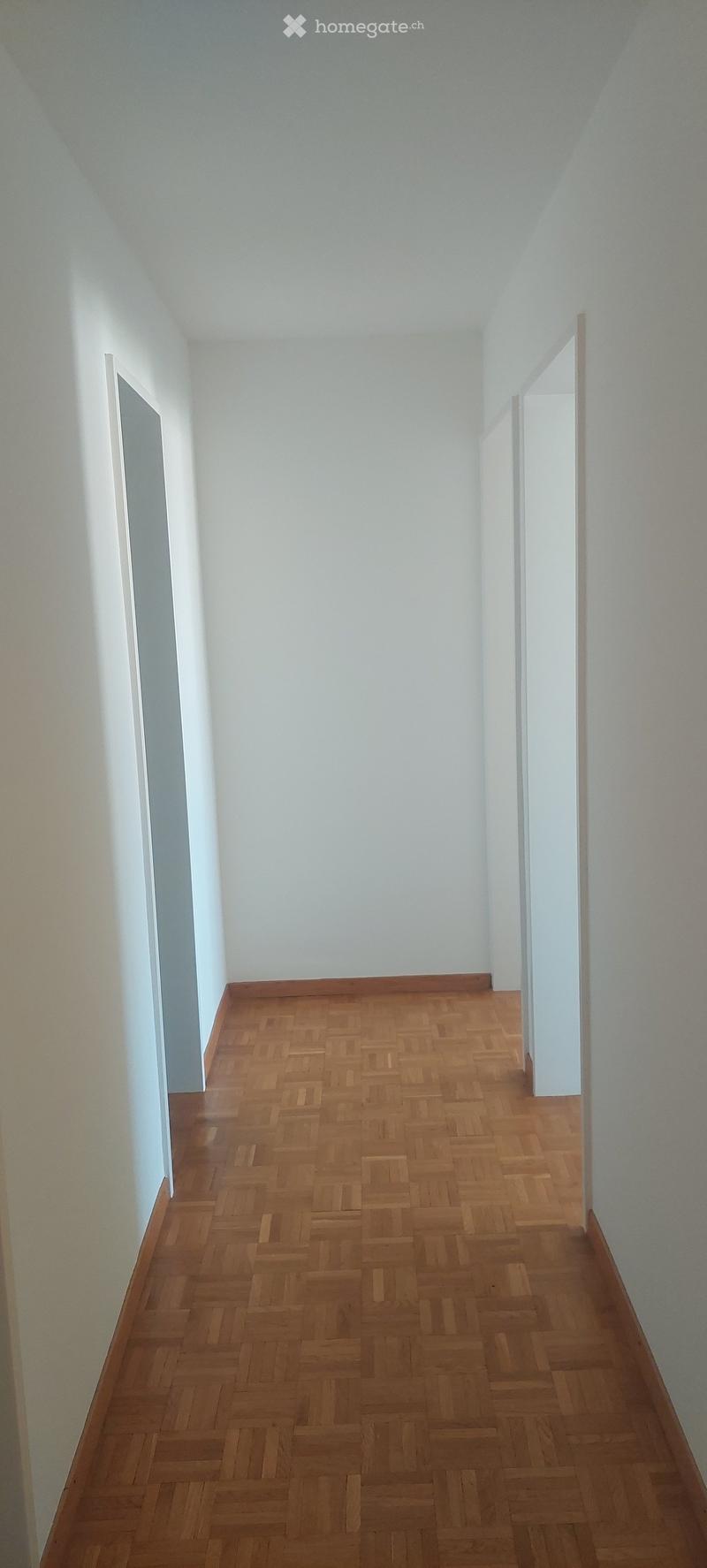 Empty hallway with wooden herringbone flooring and white walls, featuring two open doorways on either side.