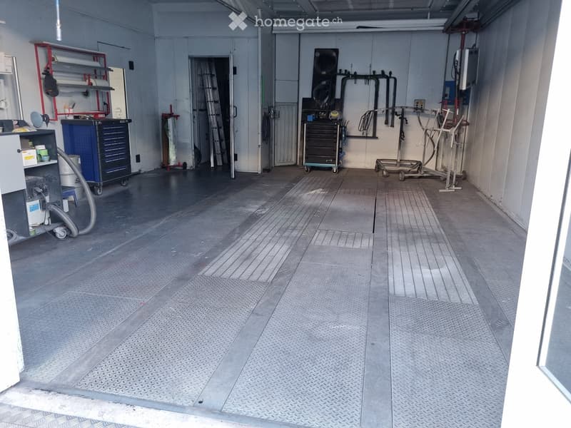 Unfurnished Room. Empty garage with metal floor, white walls, and various tools and equipment stored along the walls.