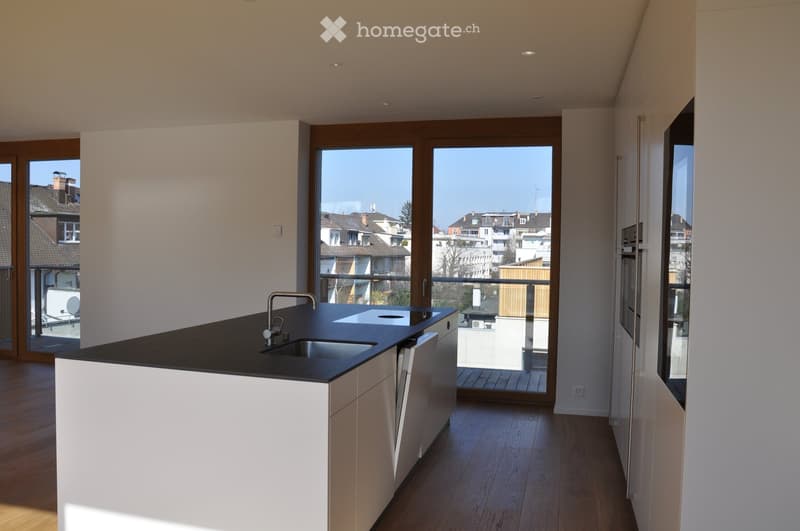 Modern kitchen with white cabinets, black countertop, and a stainless steel sink. Large windows and a balcony are visible.