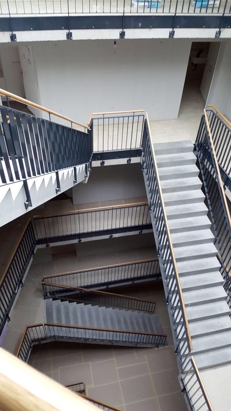 Modern interior view of a multi-level staircase with metal railings and wooden handrails, leading to an upper level.