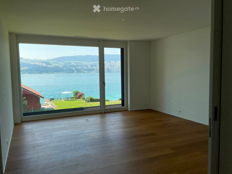 Empty room with wooden flooring, large sliding glass doors leading to a scenic view of a lake and mountains.