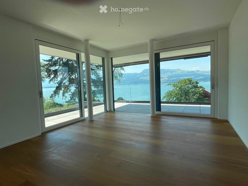 Empty room with wooden flooring, large glass sliding doors, and a scenic view of a lake and trees.