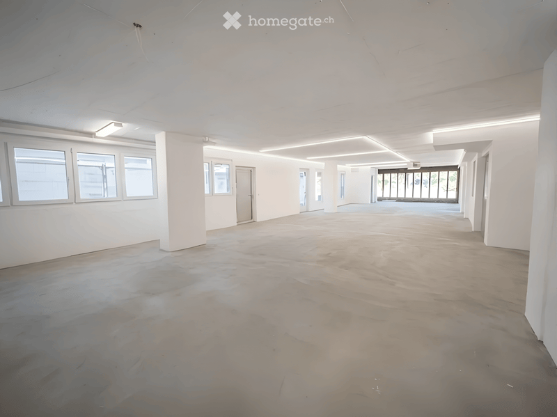 Empty room with white walls, large windows, and a concrete floor. No furniture or equipment present.