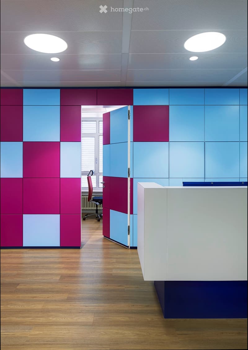 Modern office space with colorful geometric wall panels, a reception desk, and a chair in the background.