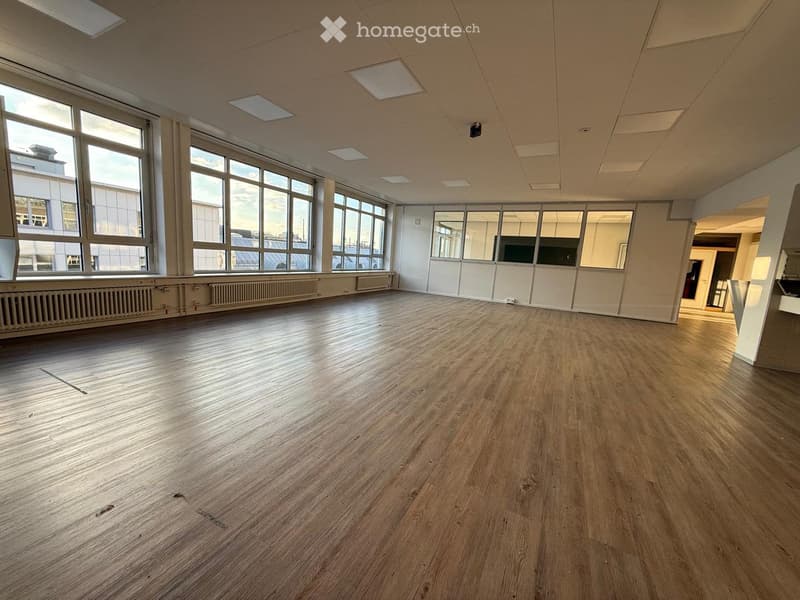 Empty room with wooden flooring, large windows, and white walls. No furniture or equipment present.