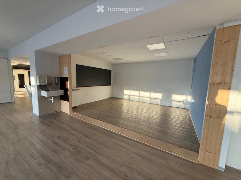 Empty room with wooden flooring, white walls, and a small sink area in the corner.