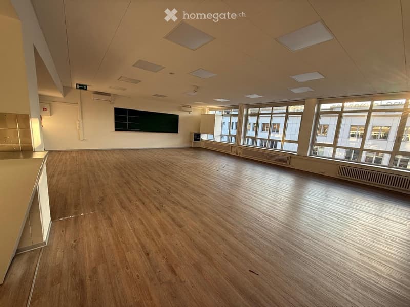 Empty room with wooden flooring, large windows, and a blackboard on the wall.