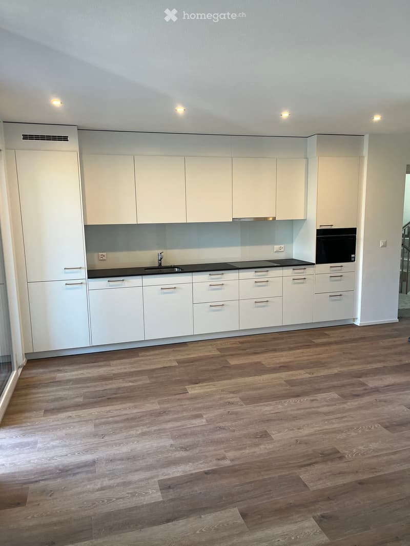 Empty kitchen with white cabinets, wooden flooring, and built-in appliances including a sink, stove, and oven. No furniture or items are present.