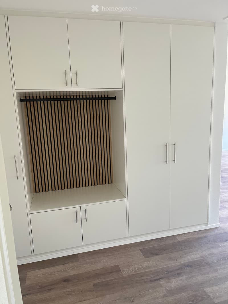 Empty room with white built-in wardrobes and a radiator, featuring wooden flooring.