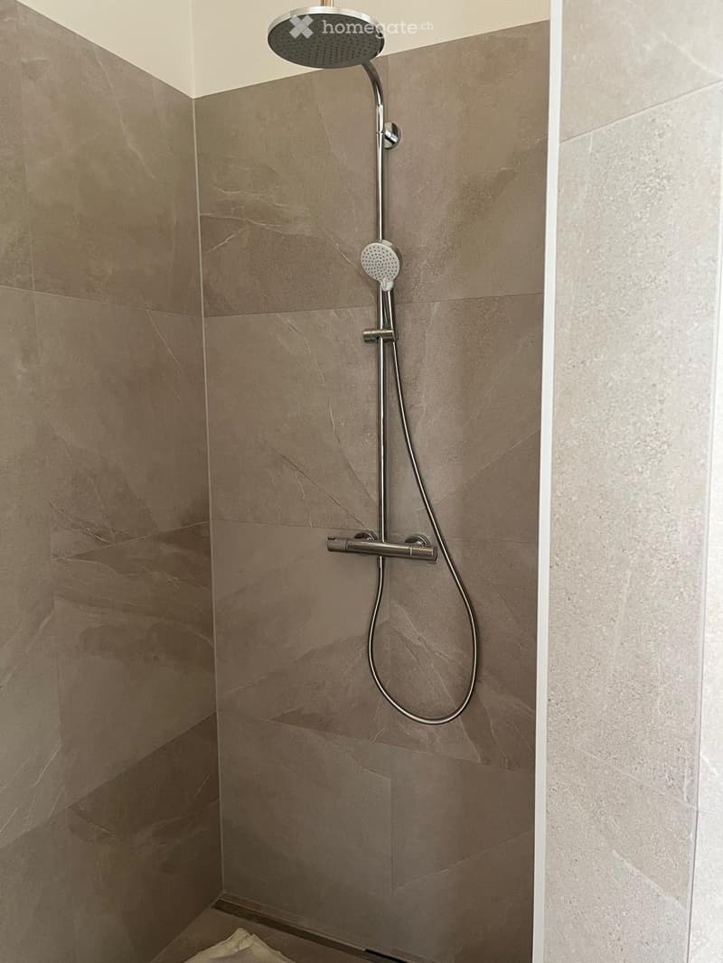 Modern shower area with a sleek, adjustable showerhead and handle mounted on beige marble tiles.