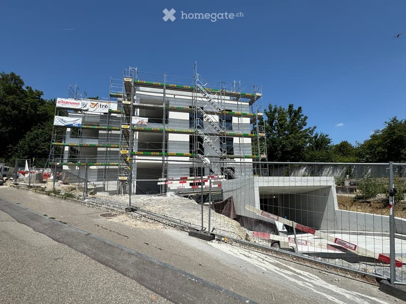 Multi-story building under construction with scaffolding, surrounded by a fenced area and construction materials.