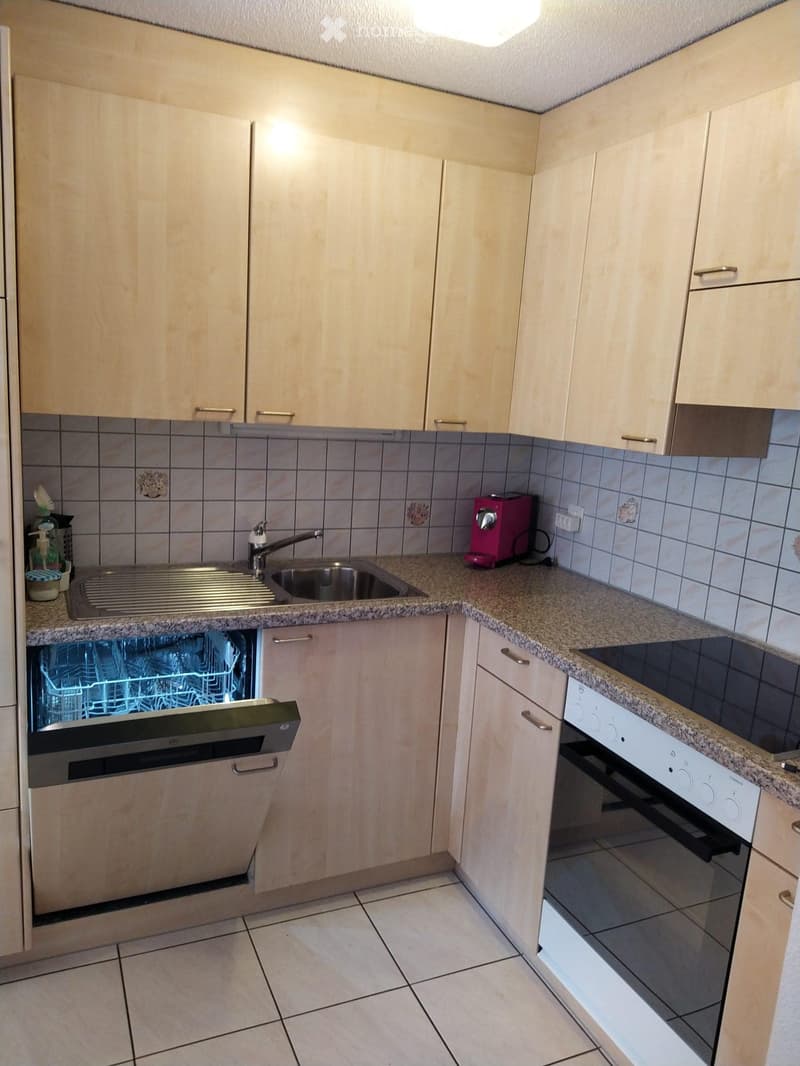 Modern kitchen with light wooden cabinets, granite countertops, stainless steel sink, dishwasher, oven, and stove.