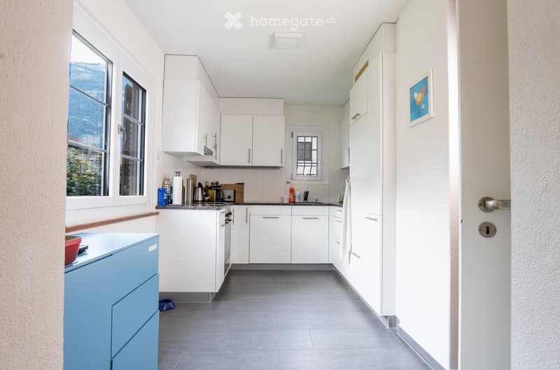 Modern kitchen with white cabinets, stainless steel appliances, and a grey tiled floor. Features a stove, sink, fridge, and a blue cabinet.