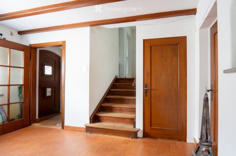 Hallway with wooden staircase, wooden doors, and tiled floor.