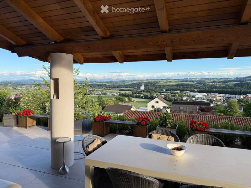 Balcony with a scenic mountain view, featuring a table, chairs, and decorative planters with flowers.