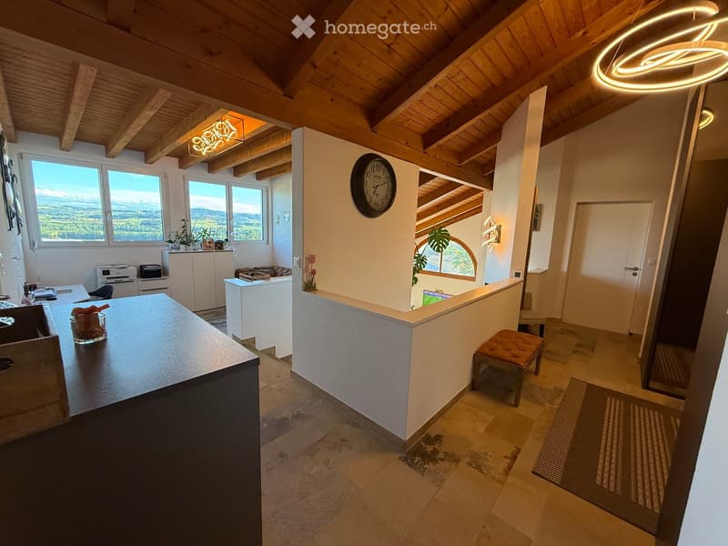 Bright, open room with wooden beams, large windows offering a scenic view, a modern table, a stool, a clock, and a cabinet.