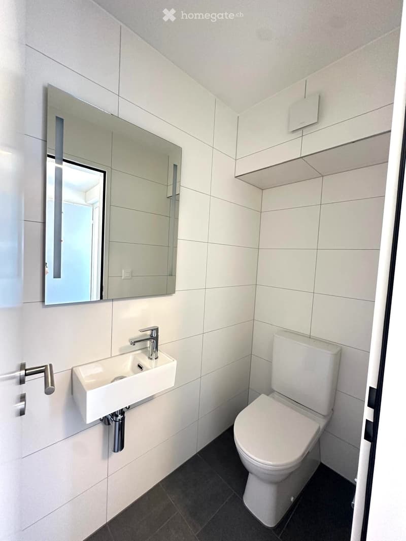 Modern bathroom with white tiles, a wall-mounted sink, chrome faucet, toilet, and a large mirror above the sink.