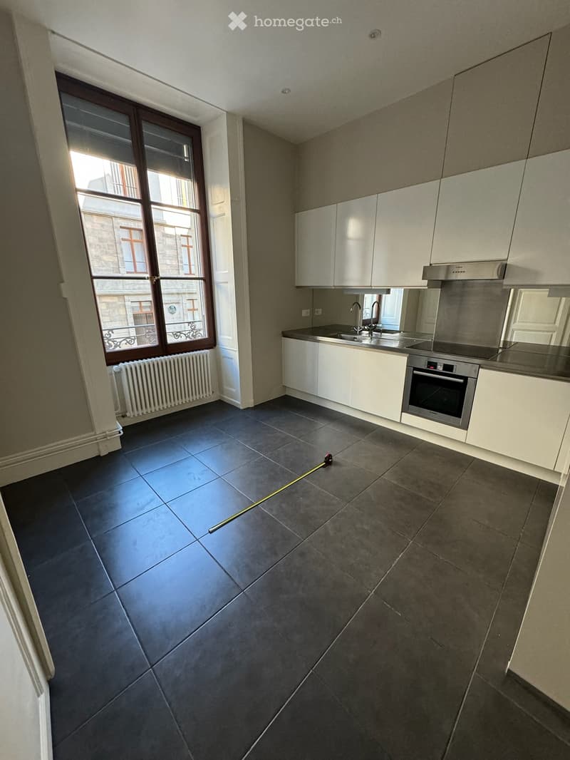 Modern kitchen with white cabinets, stainless steel sink, oven, and dark tiled floor. Large window with view of a building.