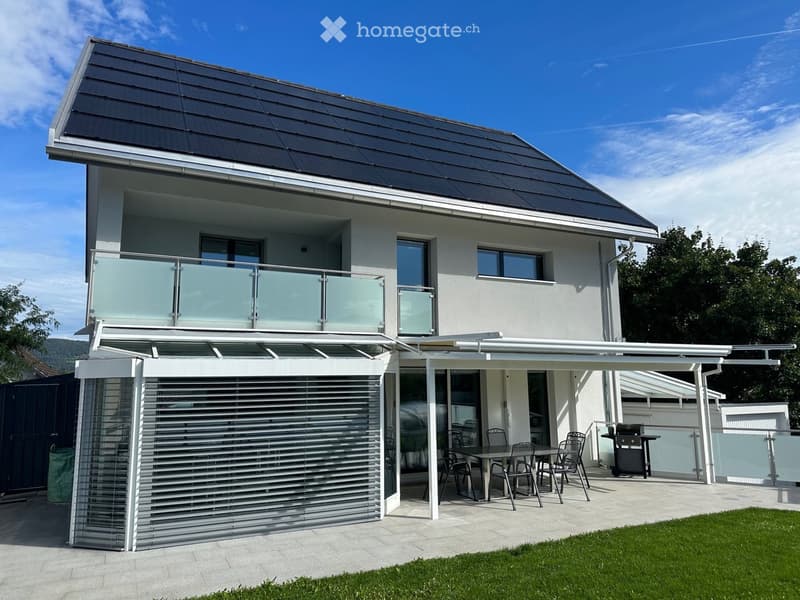 Modern two-story house with a large balcony, covered patio area, and outdoor dining setup.