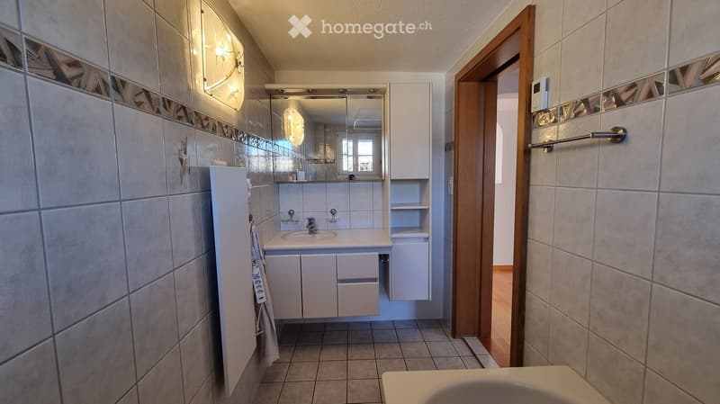 Modern bathroom with white tiled walls, a white sink with a mirror above it, and a wooden door leading to another room.