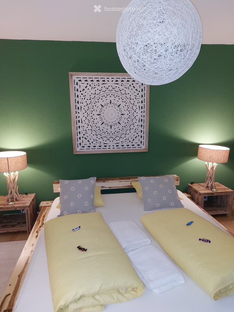 Bedroom with a large bed, decorative wall piece, two nightstands with lamps, and a round ball lamp hanging from the ceiling.