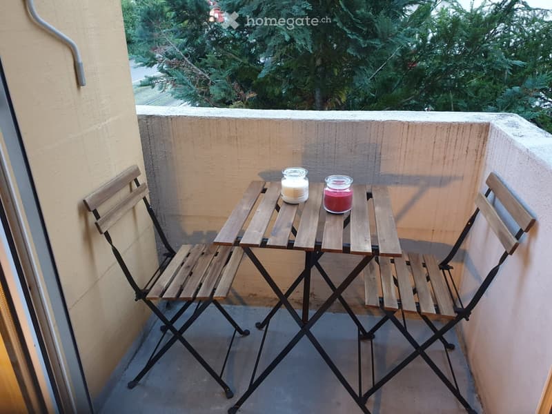 Balcony with a small wooden table and two folding chairs, two candles on the table, overlooking a green area.