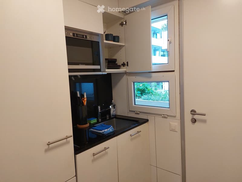 Modern kitchen with white cabinets, black countertop, built-in oven and microwave, sink with faucet, and small window above the sink.