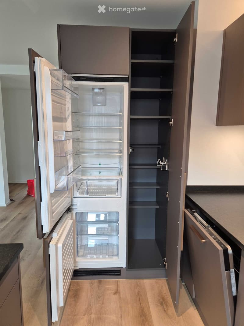 Modern kitchen with light wooden flooring, grey cabinets, and stainless steel appliances including an open refrigerator and dishwasher.