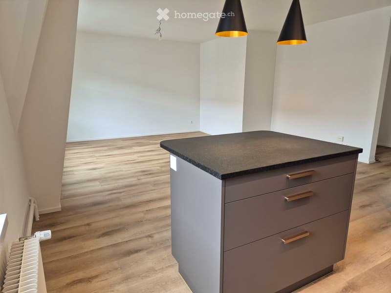 Modern kitchen with a grey island, black countertop, wooden flooring, and two pendant lights.