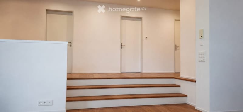 Empty hallway with wooden flooring, white walls, and three doors leading to other rooms.
