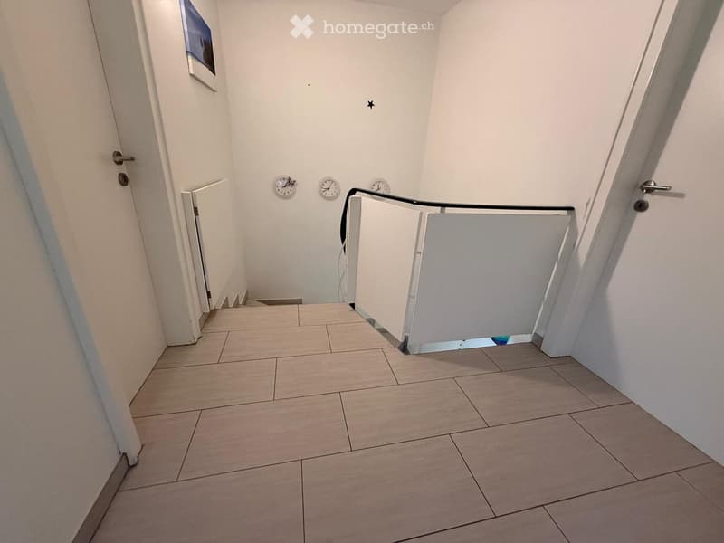 Modern hallway with tiled floor, white walls, and three wall-mounted clocks. Features a glass railing and a small open doorway leading to another area.