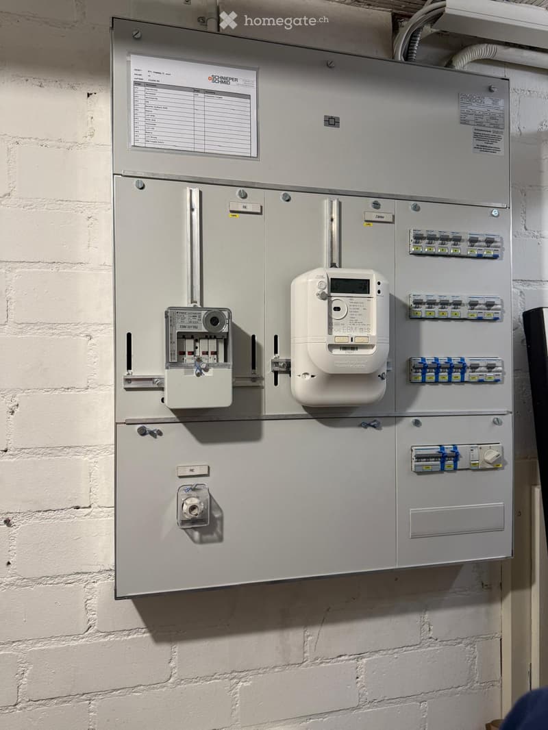 Electrical panel with meters and switches mounted on a white brick wall.